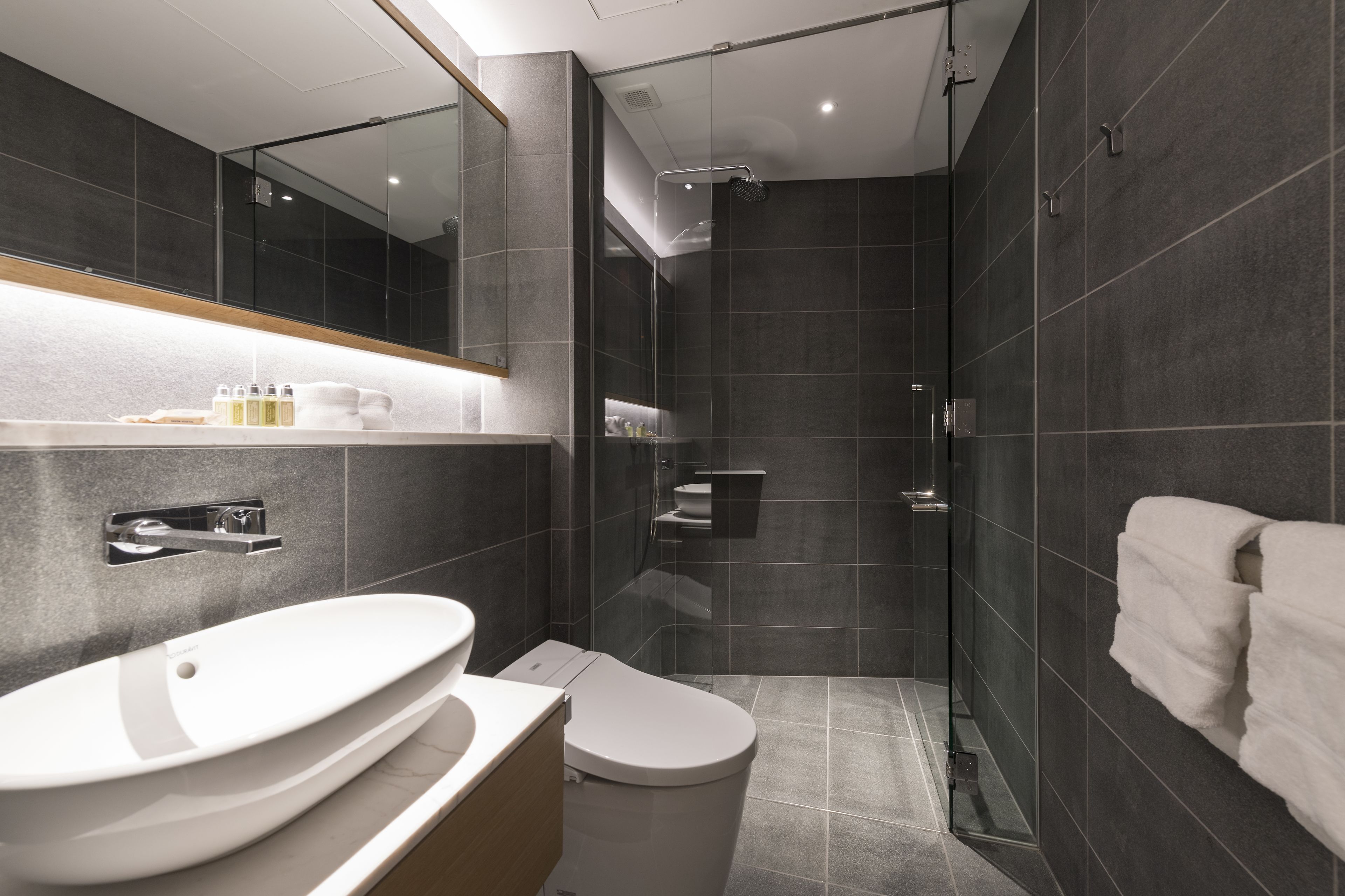 A modern bathroom with a large mirror, a white sink, a toilet, and a glass-enclosed shower area.