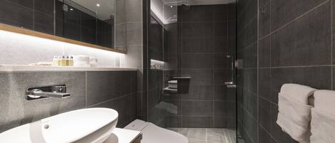 A modern bathroom with a large mirror, a white sink, a toilet, and a glass-enclosed shower area.