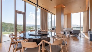 A spacious room with a round table, chairs, a sofa, and large windows offering a view of a mountainous landscape. - Skye Niseko (Kutchan)