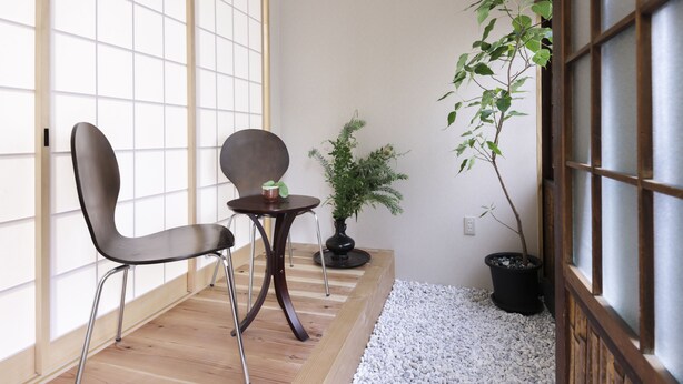 Una habitación con piso de madera, una silla negra, una pequeña mesa con una planta y otra planta en maceta cerca de una ventana con vistas.
