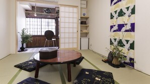 Una habitación japonesa tradicional con suelo de tatami, una mesa baja y una puerta corredera que da a otra habitación.
