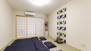 Una habitación con suelo de estera de tatami, cama futón, pantalla shoji y una pintura tradicional japonesa.