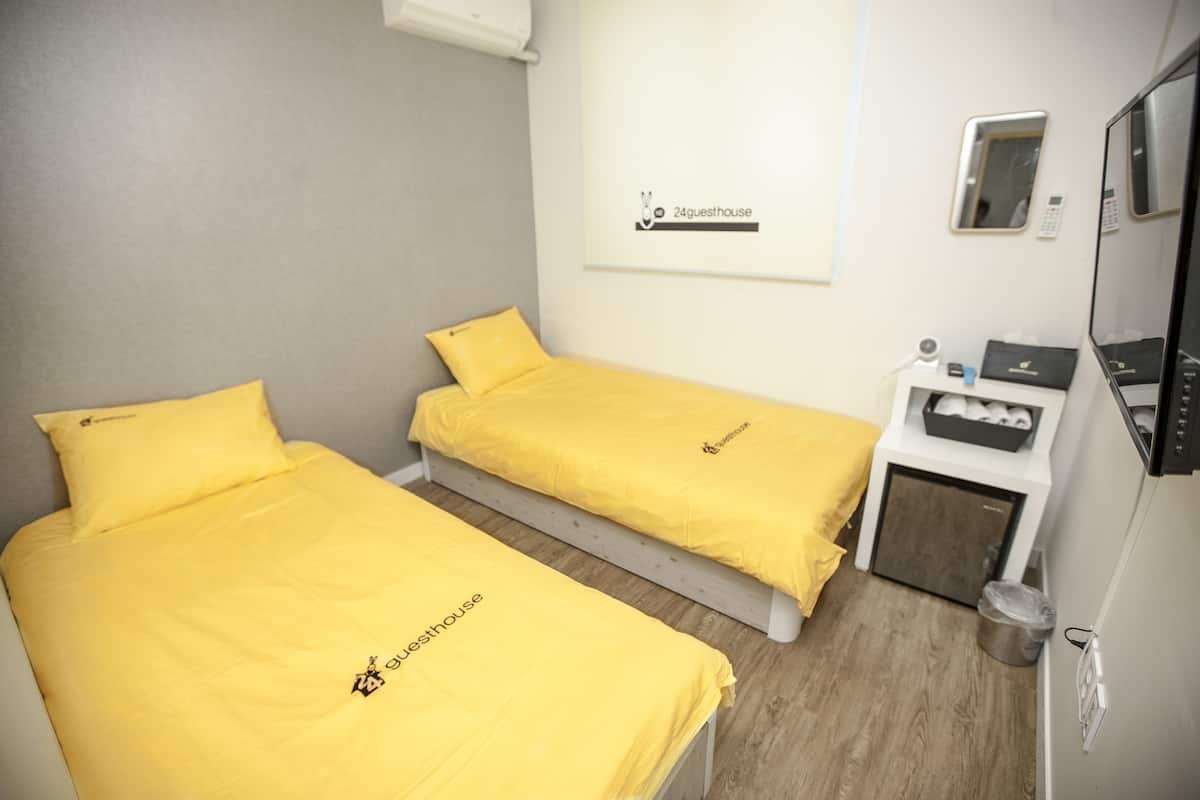 A room with two beds, each with a yellow bedspread and pillow, a small bedside table with a phone and a box, and a mirror on the wall.