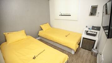 Una habitación con dos camas, cada una con cubrecama y almohada amarillos, una mesita de noche con un teléfono y una caja, y un espejo en la pared.