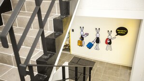 A staircase with a metal railing and a wall with cartoon rabbits holding luggage. - 24 Guesthouse Jeonju (Jeonju)