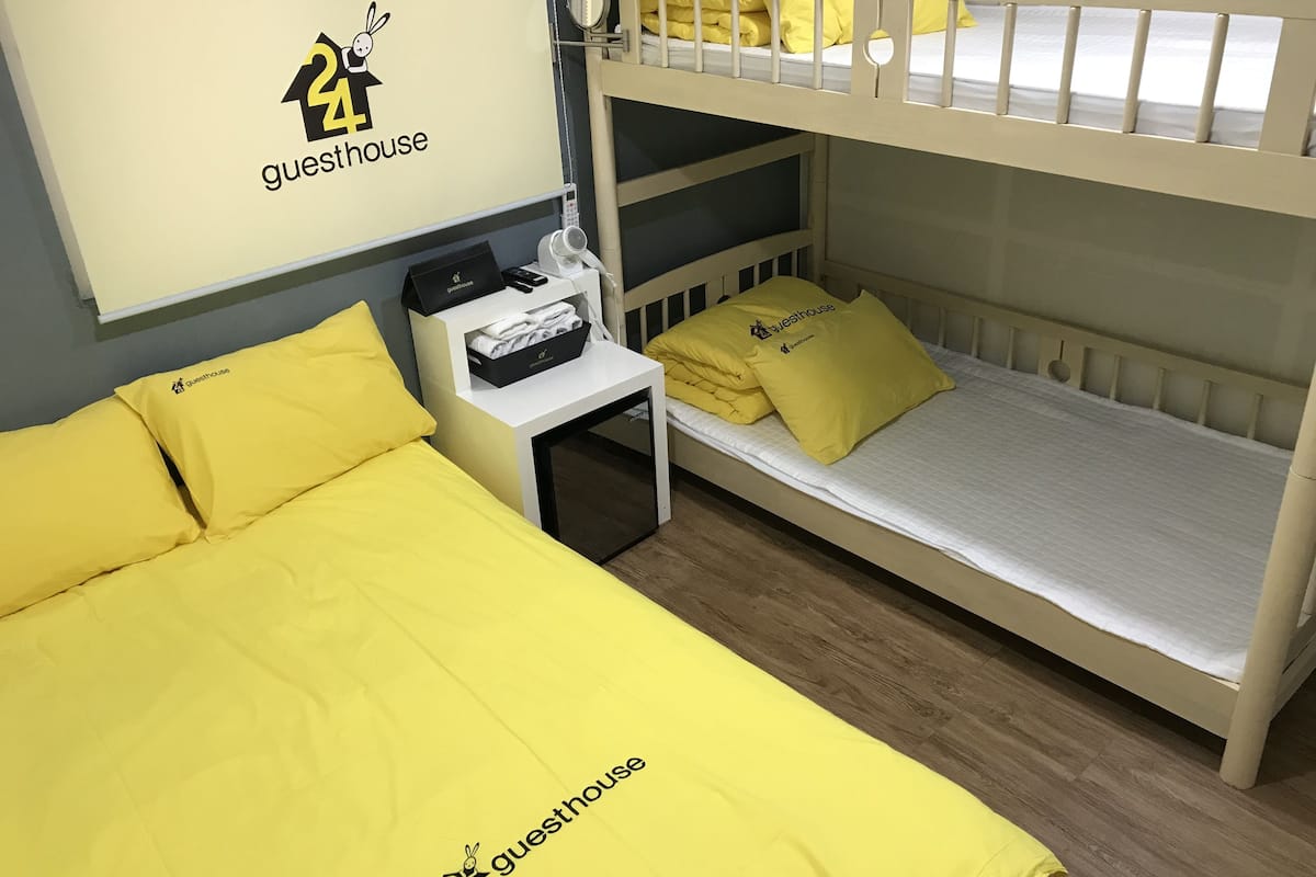 A bunk bed room with a white headboard, a bedside table with a lamp, and a wall-mounted shelf with a phone and a black bag.