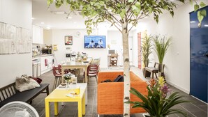 A modern living room with a dining area, a large tree, and a TV displaying a sports event. - 24 Guesthouse Jeonju (Jeonju)