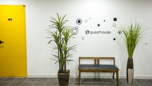 A reception area with a wooden bench, two potted plants, a yellow door, and a wall with a 'guesthouse' sign and decorative circles. - 24 Guesthouse Jeonju (Jeonju)