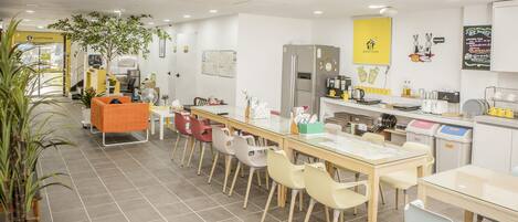 A modern kitchen with a long dining table, colorful chairs, and a refrigerator.