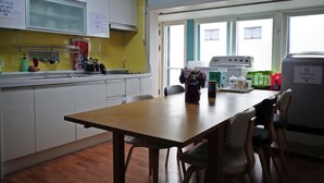 A kitchen with white cabinets, a wooden table, and chairs. There is a window with a view of the outside.
