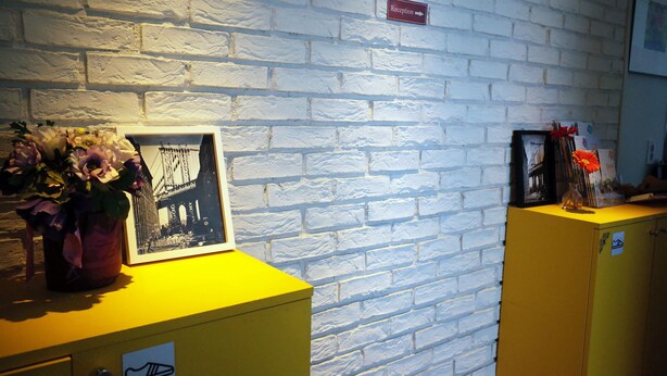 A reception area with a white brick wall, a reception sign, a framed picture of a bridge, and a yellow counter.