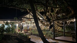 A modern outdoor area with a wooden deck, surrounded by trees and plants, and illuminated by string lights. - Coconut Beach Resort (Tavewa Island)