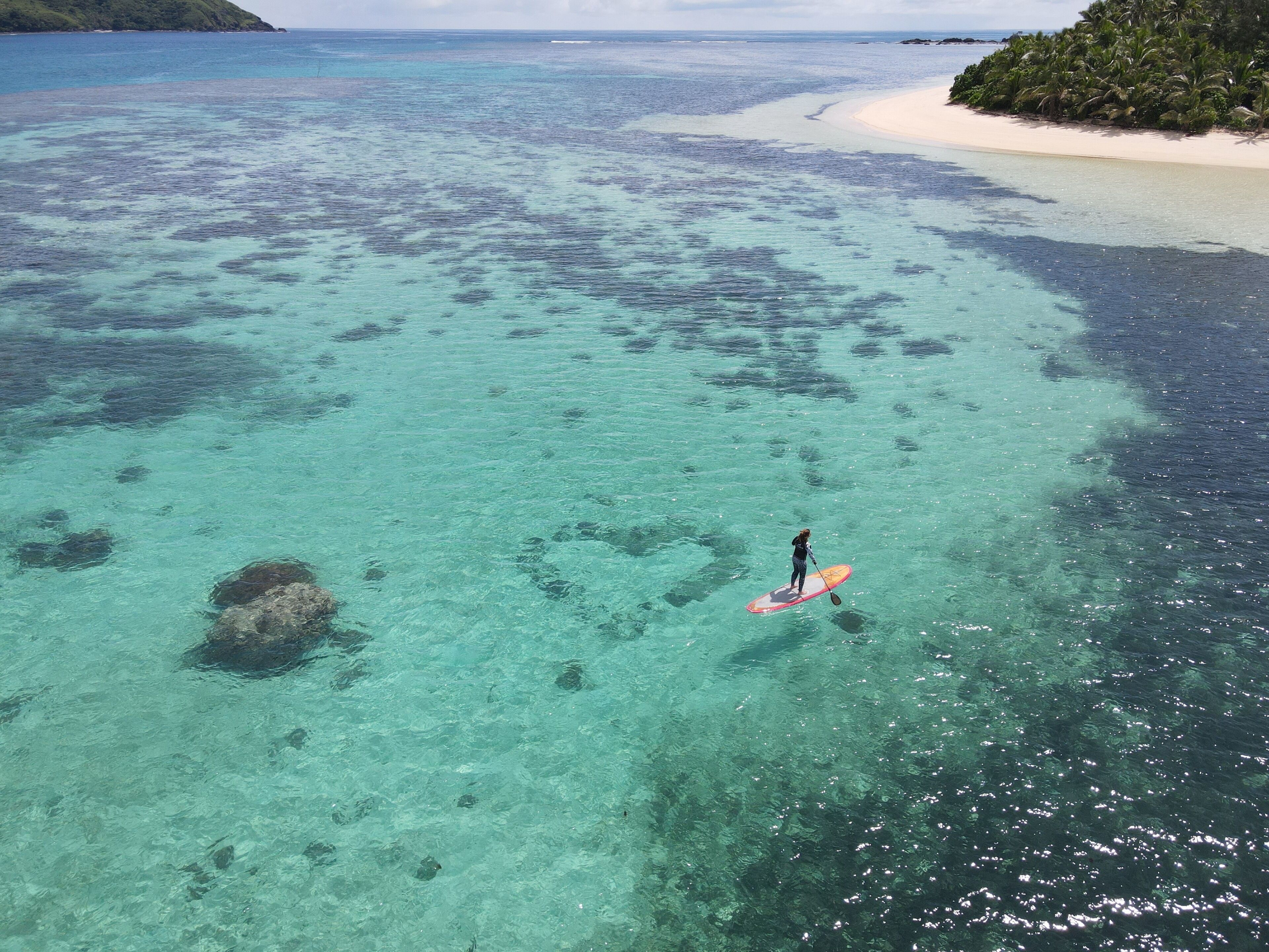 Une vue dégagée sur une plage où l’on aperçoit une personne pratiquant le stand-up paddle.