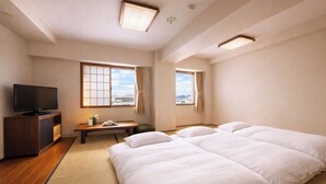 Una habitación de hotel con televisión, dos camas, escritorio y ventanas grandes.