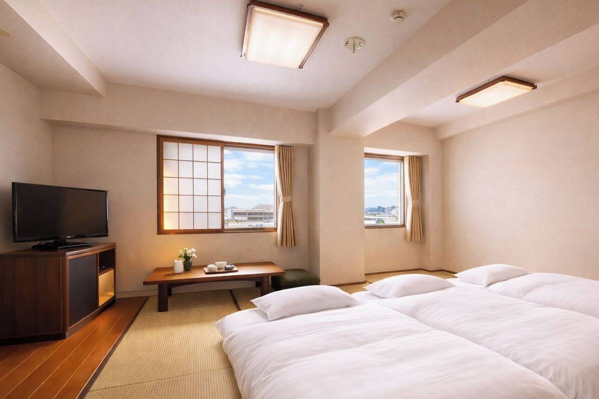 A hotel room with a TV, two beds, a desk, and large windows.