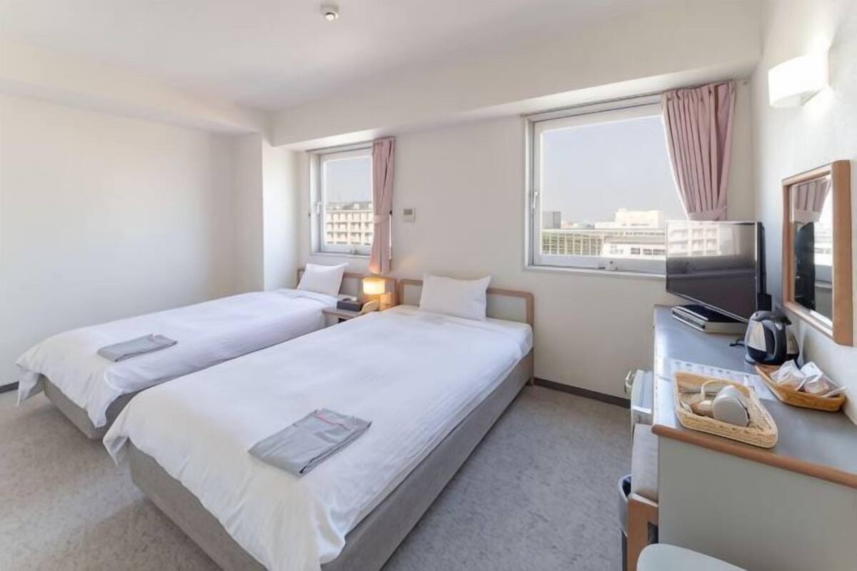 A hotel room with two beds, a desk with a computer, a TV, and a window with a city view.