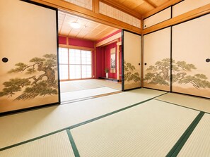 Una habitación japonesa tradicional con suelo de tatami, puertas correderas con diseños de motivos naturales y vistas a un interior rojo a través de una puerta de cristal.
