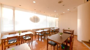 Un comedor espacioso con varias mesas y sillas de madera, ventanas grandes con vidrio esmerilado e iluminación empotrada en el techo.