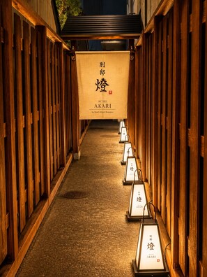 A corridor with wooden walls and a carpeted floor, leading to a banner with Japanese characters and the name 'BETTEI AKARI' by Hotel Airport Komatsu. - Hotel Airport Komatsu (Komatsu)