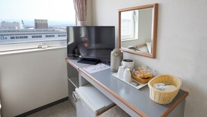 Habitación de hotel compacta con televisión, refrigerador pequeño, lavamanos, espejo y ventana con vistas a la ciudad.