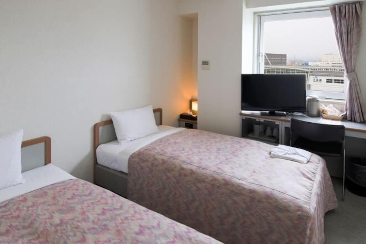 A hotel room with two beds, a desk with a television, and a window with curtains.