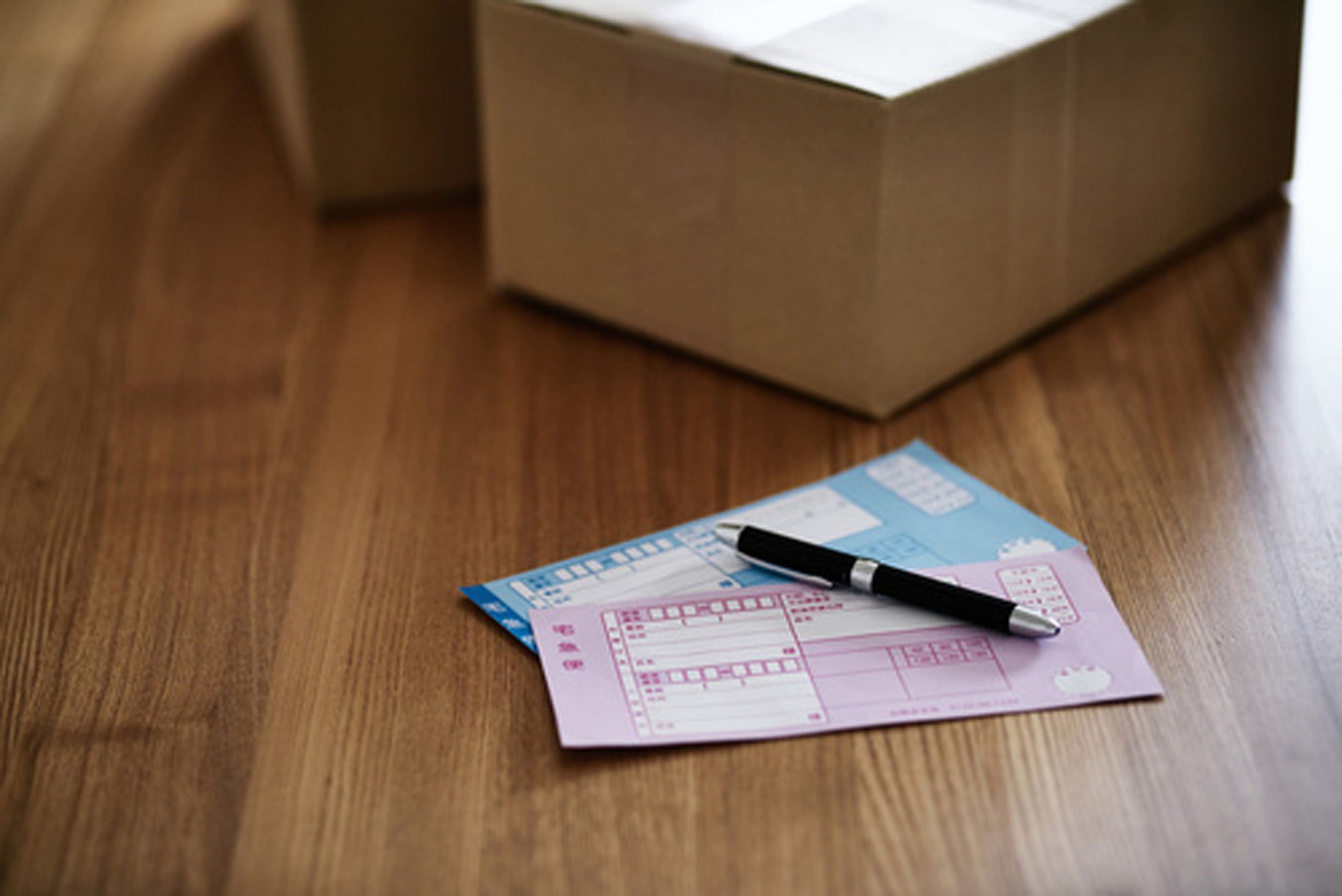 A wooden floor with a box and a pink document with a pen on it.