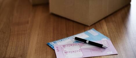 A wooden floor with a box and a pink document with a pen on it.