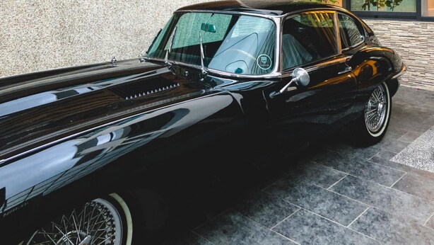 Une voiture noire classique est garée devant un immeuble dont la façade est en pierre et ornée de lambris en bois.
