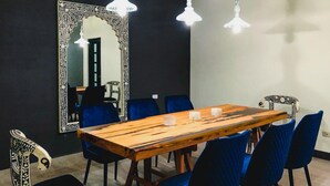 Un coin repas avec une longue table en bois, des chaises à l’assise rembourrée de couleur bleue et un grand miroir décoratif accroché au mur.