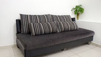 A dark grey sofa with black and white striped cushions against a white wall, with a potted plant to the right.