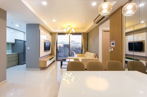 A modern living room with a large white table, beige chairs, a sofa, and a TV.