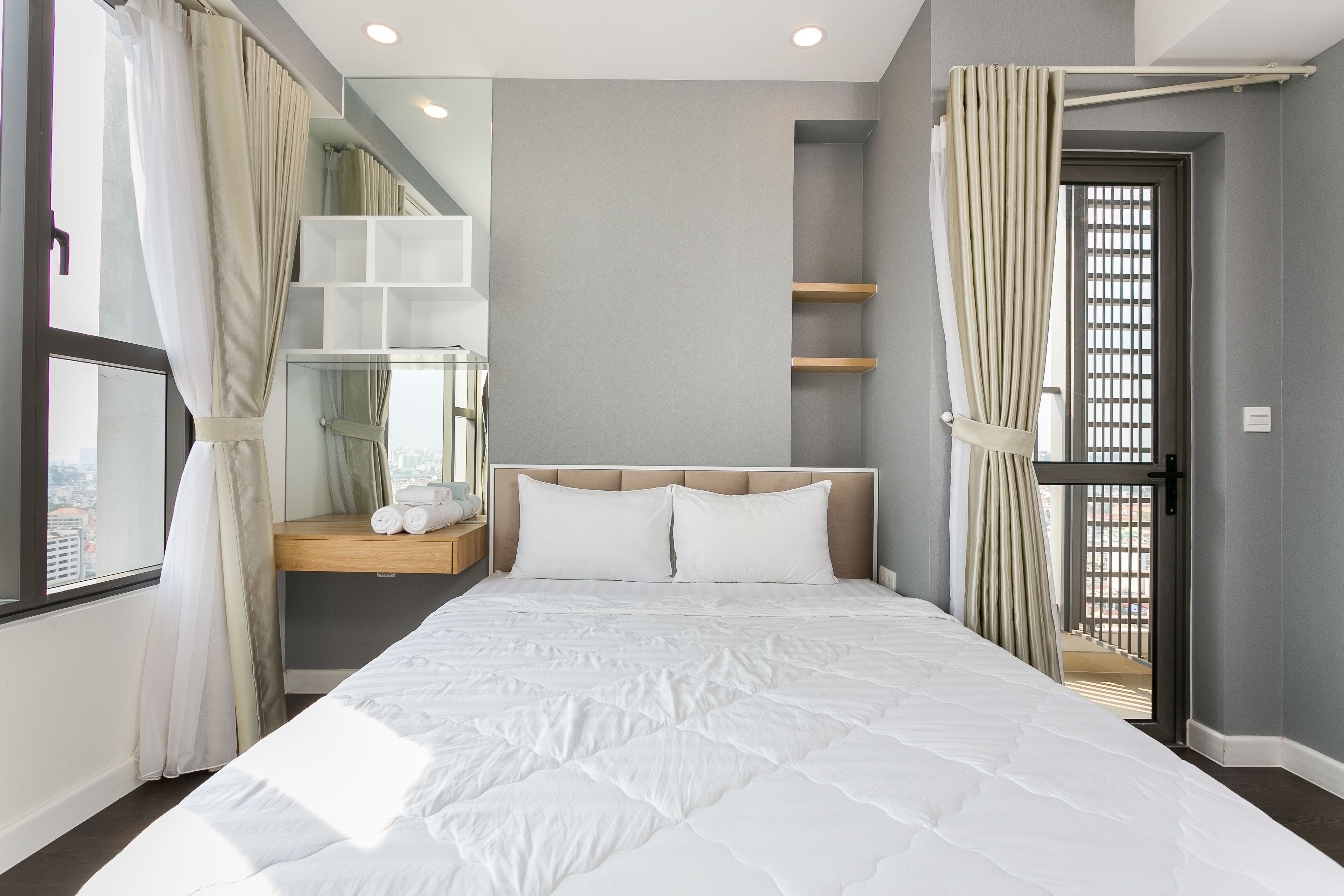 A modern bedroom with a large bed, built-in shelves, and a view of the city through the window.