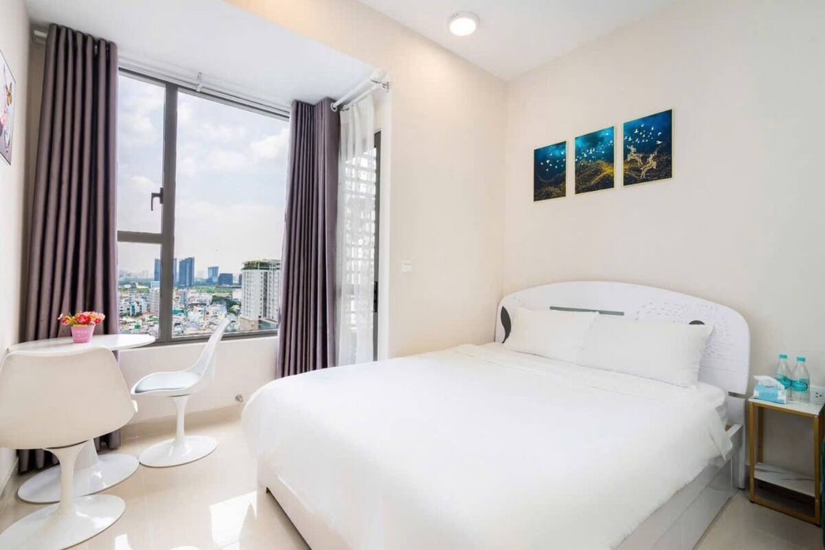 Une chambre d’hôtel comprenant un lit, un bureau, une chaise, une fenêtre avec des rideaux et deux œuvres d’art murales.