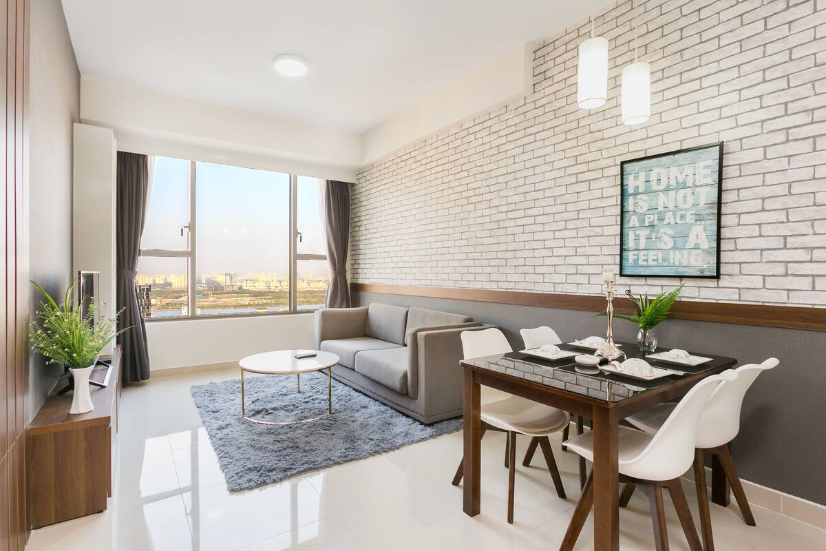Un salon moderne comprenant un canapé, une table à manger et des chaises, une grande fenêtre avec des rideaux et un mur en briques orné d’une citation inspirante.
