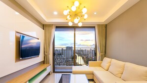 A modern living room with a flat-screen TV, a sofa, a coffee table, and a large window with a city view. - River Gate Apartment Saigon HCMC (Ho Chi Minh City)