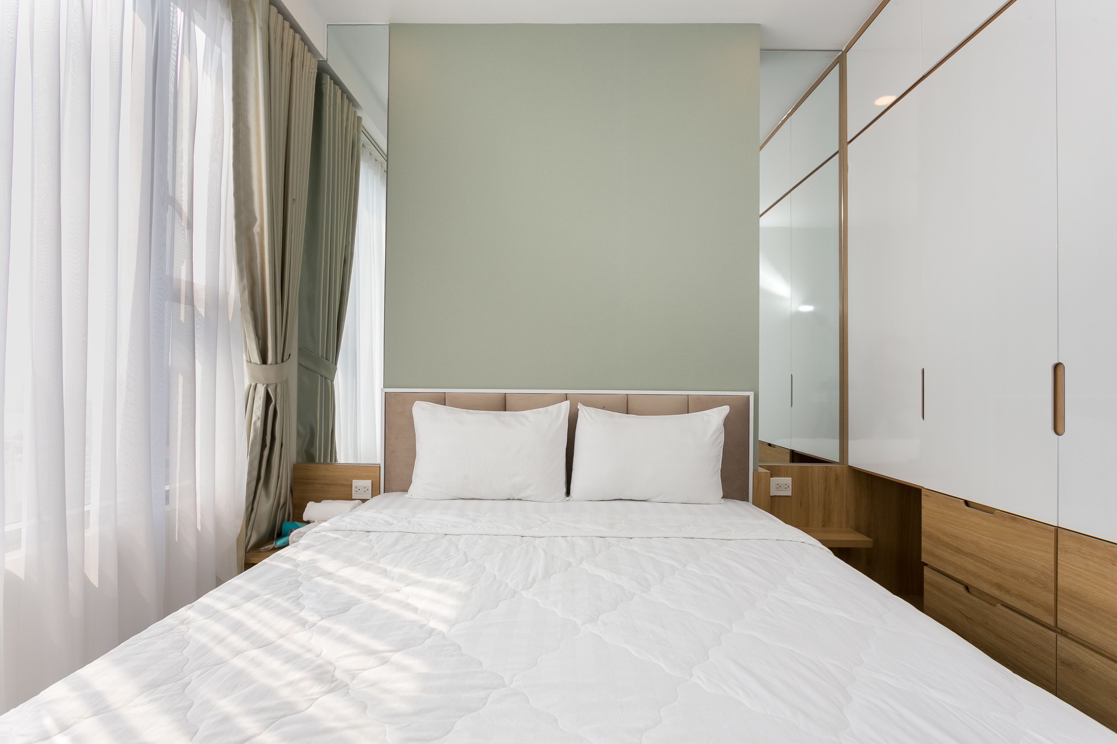 A neatly made bed with white bedding, a wooden headboard, and a nightstand with a lamp.