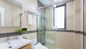 Un baño moderno con cabina de ducha de vidrio, inodoro blanco, lavamanos con mueble de madera y una planta en maceta.