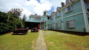 Um edifício de dois andares com um alpendre coberto, um caminho de pedra que leva à entrada e uma pequena árvore no centro.