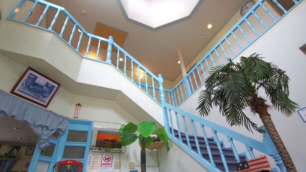 Interior com vários níveis, uma escadaria central, mobiliário de madeira e uma grande planta.