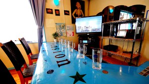 Uma área de bar com uma mesa azul identificada como "Tension", copos e uma tela de TV exibindo um programa.