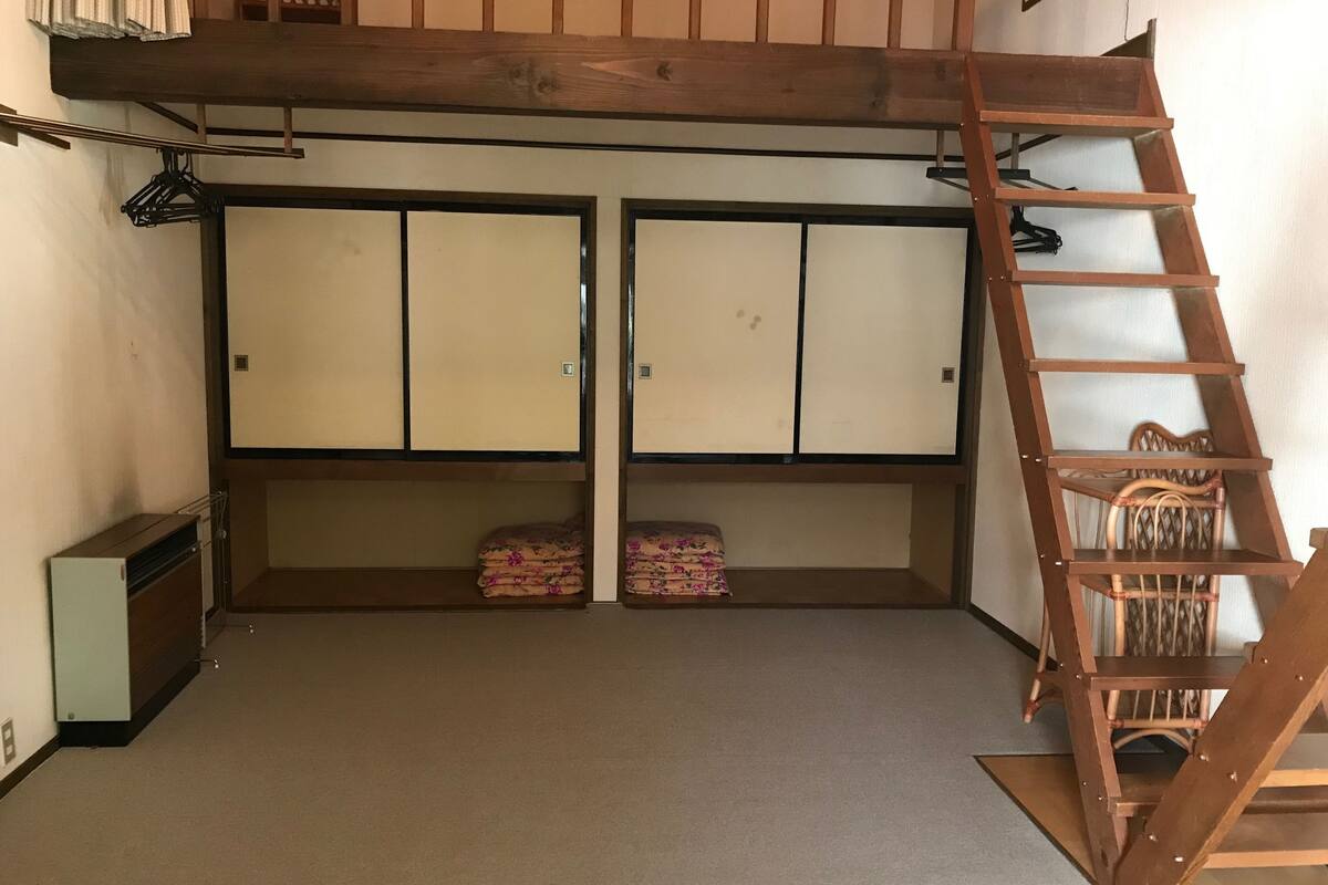 A room with a bunk bed, a ladder, and a chair. There are two cabinets and a small table.