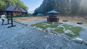 Ein Kiesplatz mit einer Holzterrasse, einem überdachten Sitzbereich und einem Gebäude mit Satteldach.