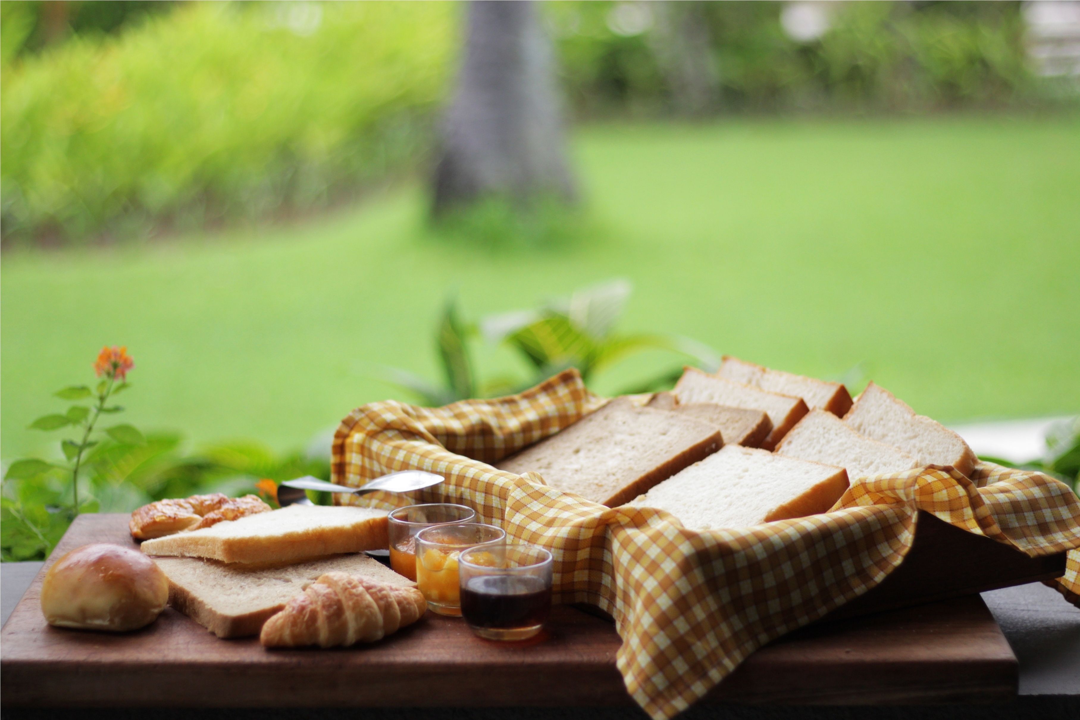 En picknickuppsättning med bröd, croissanter och drycker på ett träbord utomhus.