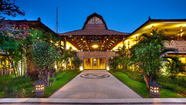 A large, well-lit building with a central entrance, surrounded by lush greenery and stone pathways. - Mangsit Suites by Holiday Resort Lombok (Senggigi)