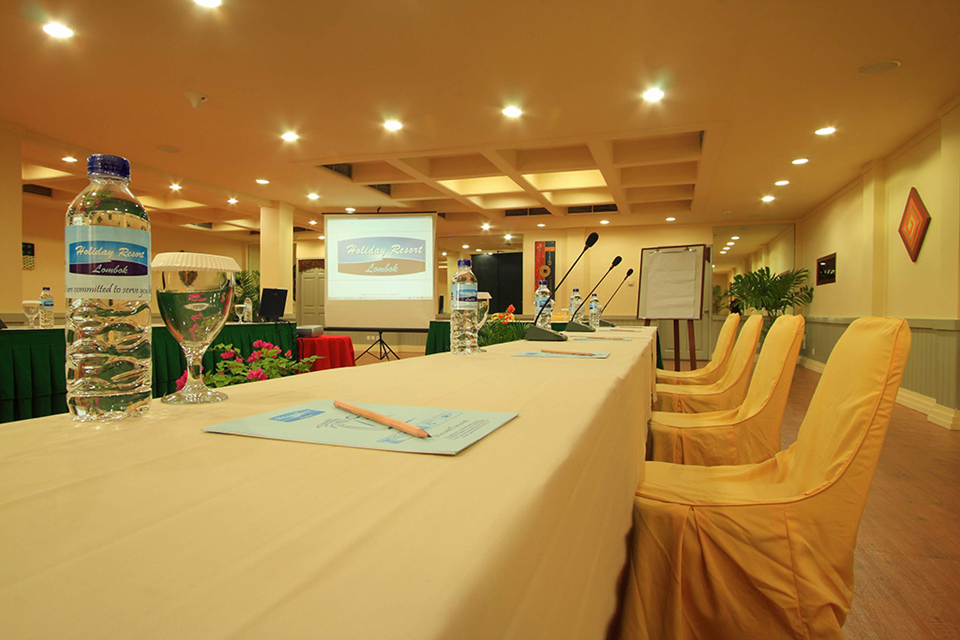 A conference room with a long table, chairs, a projector screen, and a water bottle.