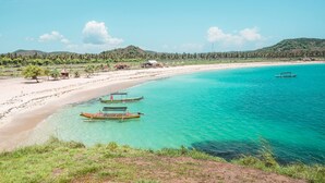 A beach with clear turquoise waters, several boats, and a few small huts. - Mangsit Suites by Holiday Resort Lombok (Senggigi)