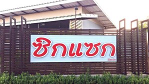Ein Schild mit thailändischen Schriftzeichen an einer Gebäudefassade.