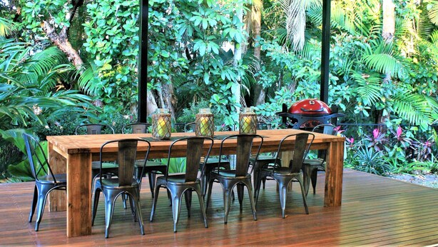 Una terraza de madera con una mesa y sillas, rodeada de abundante vegetación.