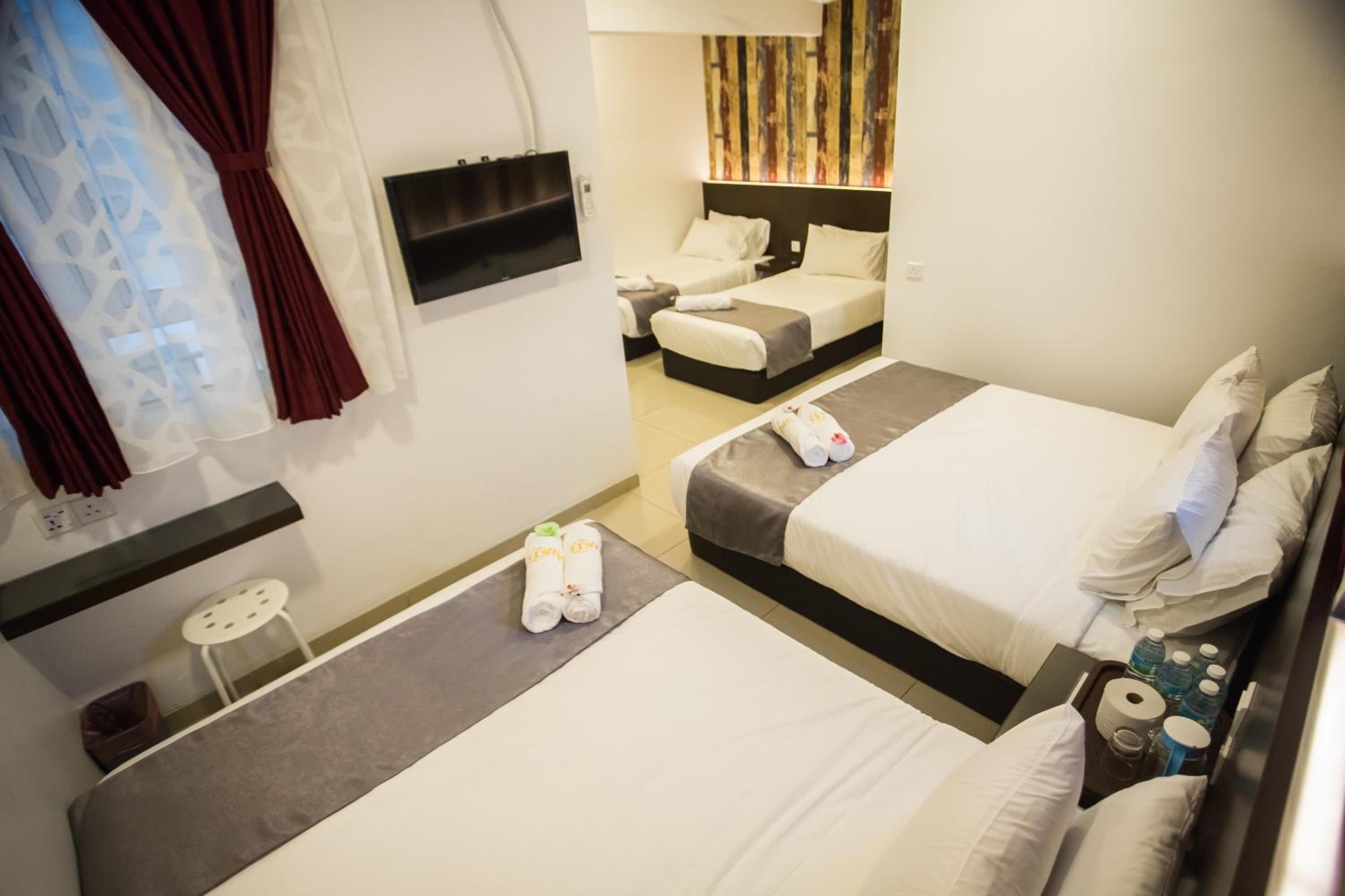 A hotel room with two beds, a TV, a small table, and a wall-mounted shelf.