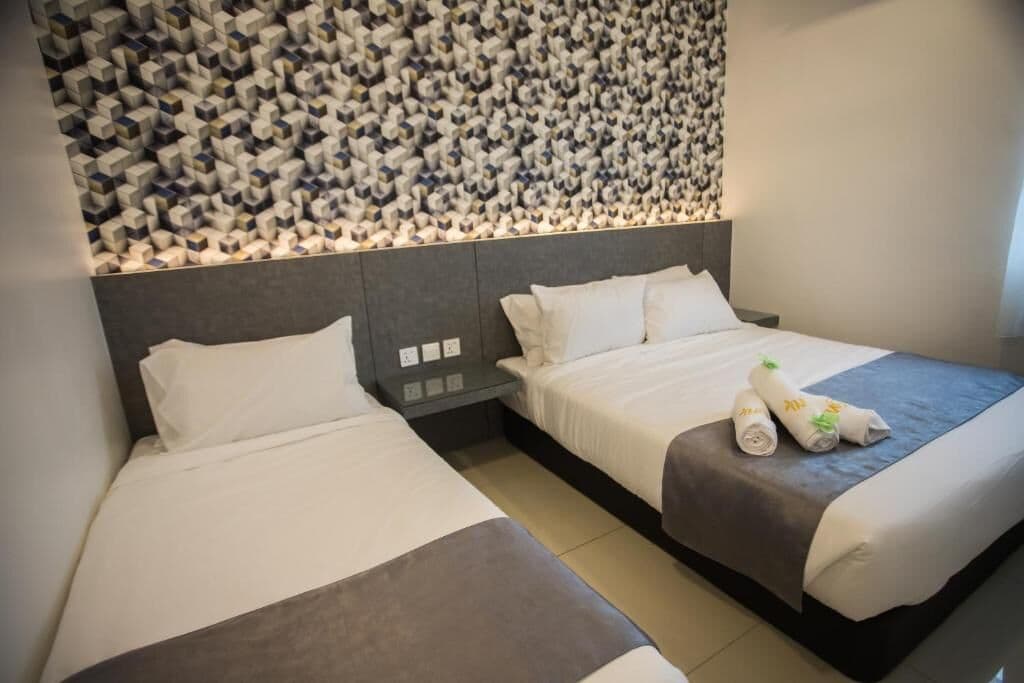Habitación de hotel con dos camas, un diseño de pared moderno y una cama bien tendida con toallas.
